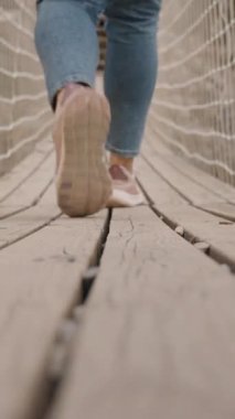 Dikey video. Derin Kayalık Kanyon 'un Üzerinde Asılı Halat Köprüsü Üzerinde Yürüyen Bir Kadının Arka Görünümü Düşük Açı, Korku ve Heyecan Konseptinden Yakalandı