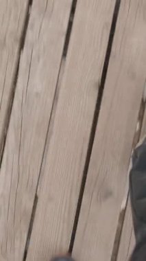 Dikey video. Tahta askı köprüsünde siyah pantolon ve siyah bir spor ayakkabı giyerek yürüyen birinin birinci şahıs görüntüsü. Bulanık hareket hareket ve yüksekliği gösteriyor.