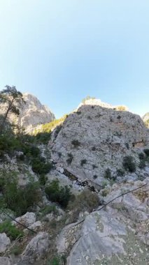 Dikey video. Derin Kanyon 'da Büyük Rocky oluşumunun Manzarası, Yeşil Ağaçlar ve Vadi' de akan küçük bir nehirle çevrili, Parlak Mavi Gökyüzü Altında, Geniş Açı