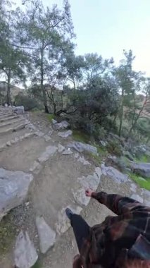 Dikey video. Ağaçlar ve kayalarla çevrili, 360 derecelik kamerayla çevrili, Ormanlı Dağ Yolu 'ndaki Taş Merdivende Yürüyen Küçük Gezegen Efekti