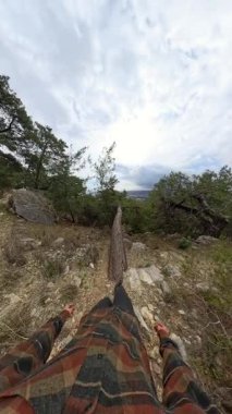 Dikey video. Düşen Ağaç Gövdesinin Üzerinde Dengelenen Bir Adamın İlk Görüş Alanı Dağlık bir manzaraya bakan Bulutlu Gök Altındaki Şehir