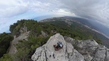 Uçurumun kenarında oturan bir çift. Deniz manzaralı bir selfie çekiyorlar. Ve dramatik bulutlu bir gökyüzü altında uzak bir şehir.