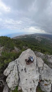 Dikey video. Uçurumun kenarında oturan bir çift. Deniz manzaralı bir selfie çekiyorlar. Ve dramatik bulutlu bir gökyüzü altında uzak bir şehir.