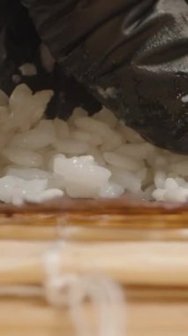 Dikey video. Düşük açılı Makro Bir Eldiven Çekimi Siyah Eldivenli Yapışkan Suşi Pilavı Bir Norveç çarşafına basıyor Kamera Bambu Mat boyunca ileri doğru kayıyor