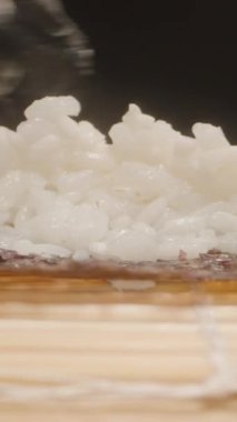 Dikey video. Siyah Eldiven Giyen Bir Elin Makro Yakın Çekimi Nori Çarşafı Üzerindeki Suşi Pirincini Eşit Dağıtırken, Kamera Bambu Çukuru boyunca Hareket Ederken, Süreci Vurguluyor