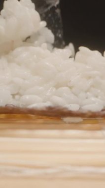 Dikey video. Siyah Eldiven 'i dikkatle teslim et Yapışkan Suşi Pilavını Nori çarşafının üzerine sererken Kamera Mat boyunca Detaylı Makro Çekim yaparken