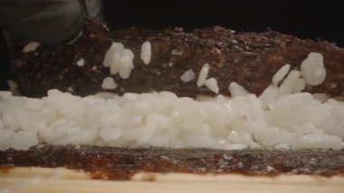 Yapışkan suşi pilavının üzerine nazikçe Nori çarşafı katlayarak suşi yapma sürecinin makro yakın plan çekimini ele geçirmek.