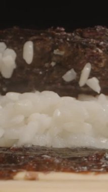 Dikey video. Yapışkan suşi pilavının üzerine nazikçe Nori çarşafı katlayarak suşi yapma sürecinin makro yakın plan çekimini ele geçirmek.