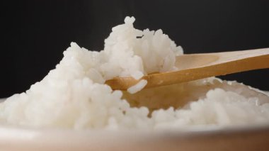 Tahta kaşık kaldırma Buharlı Taze Pişmiş Beyaz Pirinç Kaseden, Yumuşak Doku ve Nemlendirmeyi Gösteren Karanlık Bir Arkaplana Karşı Sıcak Buharda Yükseliş