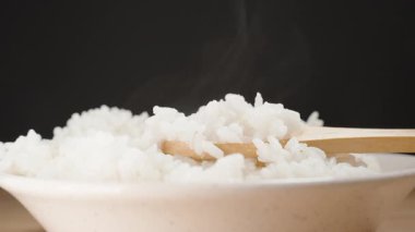 Bir kase taze pişmiş beyaz pirinç üzerine yükselen buhar bir tahta kaşık gibi yumuşak ve nemli tahıllar sıçrıyor, sıcak ve rahatlatıcı bir sahne yaratıyor