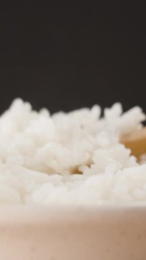 Dikey video. Tahta bir kaşıkla el ele tutuşmak Buharda pişen beyaz pirinci kaseden çıkarmak, Nemli Tanelerle Isıyı ve Yumuşak dokuyu yakalamak