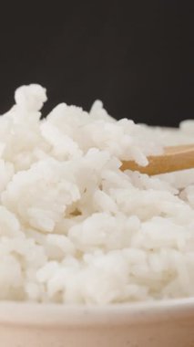 Dikey video. Bir Elin Yakın Çekimi Bir Ahşap Kaşık Kullanarak Taze Pişmiş Beyaz Pirinci Buhar Kâsesinden, Yumuşaklığı ve Sıcaklığı Vurguluyor