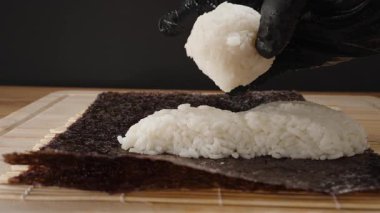 Siyah Eldivenli Yapışkan Beyaz Pirinçli Kalın bir katmanı Nori çarşafına bastırıp Suşi Roll 'u özenle ve titizlikle hazırlıyor.