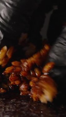 Dikey video. Siyah Eldivenli Eldiven Yapışkan Beyaz Pirinç 'i Norveç çarşafı üzerinde Soya Sosu ile karıştırarak Koyu, Cilalı ve Bol Baharatlı Pirinç Dokusunu Yaratıyorlar.