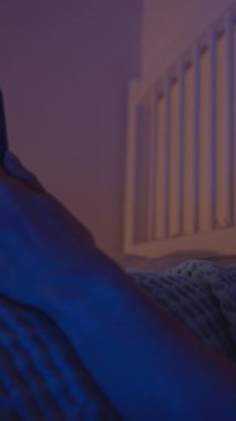 Dikey video. Yatakta Yatan Kadın Akıllı Telefon ve İçerik, Yan Görünüm, Duygusal Gece Konsepti izlerken Gülmekten Gözyaşlarını Siliyorum