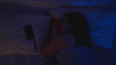 Mavi Işık Altında Yatakta Dönen Bir Kadın Sonra Yastığının Yanındaki Akıllı Telefona Uzanıyor, Üst Görüş, Uykusuzluk Konsepti