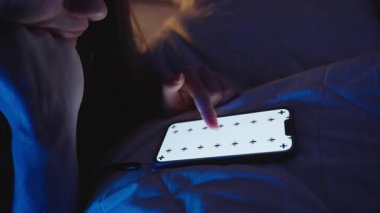 Gece Yatakta Mavi Ortam Işığı, Kapalı Yan Açı, Uyku Öncesi Kaydırma Konsepti ile İzleme İşaretleri Ekranda Kaydıran Akıllı Telefonlu Kadın Dinleniyor