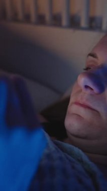 Dikey video. Yataktaki Yorgun Kadın Akıllı Telefonu Sıyırdı ve Gözleri İki Elle ovuşturdu Gece Sosyal Beslemeden Sonra, Mavi Ortam Işığıyla Yan Açı, Ekran Yorgunluğu Konsepti