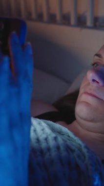 Dikey video. Gece Parlak Akıllı Telefon Ekranı 'ndan Yataktaki Kadın Göz Süzme ve Grimating Kamera Yavaşça Sönük Odasında Yastığa Düşerken, Göz Solukluğu Konsepti