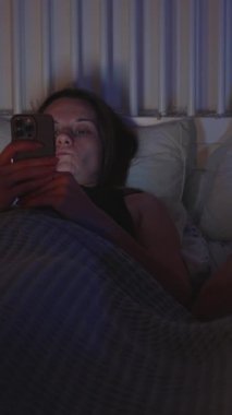Dikey video. Kadın ve Erkek Gece Yatağında Uzanıyor Mavi ve Sıcak Işıklı Akıllı Telefonları Kullanıyor, Kaypak Vuruşu, Dijital Bağlantısızlık Konsepti