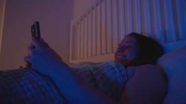 Yatakta Yatan Kadın Akıllı Telefon ve İçerik, Yan Görünüm, Duygusal Gece Konsepti izlerken Gülmekten Gözyaşlarını Siliyorum