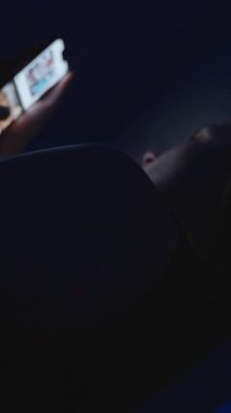 Dikey video. Gece Yatağında Yatan Kadın Düşük Açı, Dijital Bağımlılık Konseptinde Ekran Işığından Akıllı Telefon Kullanıyor