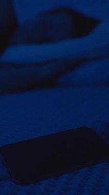 Dikey video. Gece Yatağında Yatan Kadın Telefonuna Uzanıyor ve Sahtekarlık, Düşük Işık Sahnesi, Ekrana Yakın Odaklı, Dijital Güvenlik Konseptine Odaklanan Çağrıyı Reddediyor