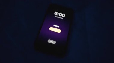 Alarm sabah 5 'te çalmaya başlıyor. Kadın, onu kapatmak için Karanlıktaki Akıllı Telefona, Ekran Işıklandırılmış, Yakın-Yakın-Düşük Açılı, Şafak öncesi Uyanış Konsepti' ne uzanırken...
