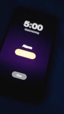 Dikey video. Alarm sabah 5 'te çalmaya başlıyor. Kadın, onu kapatmak için Karanlıktaki Akıllı Telefona, Ekran Işıklandırılmış, Yakın-Yakın-Düşük Açılı, Şafak öncesi Uyanış Konsepti' ne uzanırken...