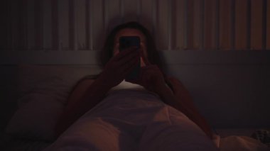 Loş Odada Yatakta Yatan Bir Kadın İki Elle Akıllı Telefonu Tutarak ve Uykudan Önce Gözden Geçirerek, Ön Görüş, Dijital Yatma Zamanı Konsepti