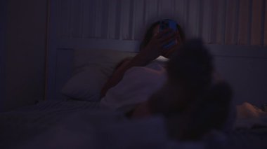 Kadın Smartphone 'a Bakar Ayaklarıyla Yatakta Uzanırken Kameraya doğru, Loş Aydınlatma Odasında, Yakın-Yakın-Düşük Açı, Rahatlatıcı Akşam Konsepti