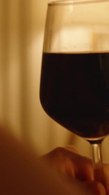 Dikey video. Sıcak Ortam Işığında Kırmızı Şarabı İçen Kadın Parmaklar ve Cam Köküne Odaklanıyor, Akşam Gevşemesi Kavramı