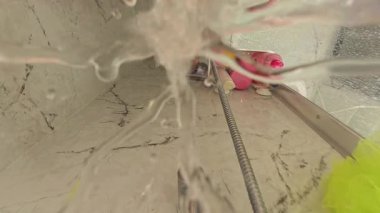 Dikey video. Su Damlaları Kamera Merceğine Sıçrıyor Duş zemininin yakın görüntüsünde Banyo Oyuncakları ve Şampuan Şişeleri Arkaplanda Duş Yenileme Sahnesinde