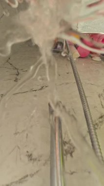 Dikey video. Su Damlaları Kamera Merceğine Sıçrıyor Duş zemininin yakın görüntüsünde Banyo Oyuncakları ve Şampuan Şişeleri Arkaplanda Duş Yenileme Sahnesinde