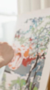 Dikey video. Sanatçı Fırça Dönüşü Yumuşak Işık ve Bulanık Arkaplan, Yan Açı, Yaratıcı Akış Konsepti ile Renkli Ağaç Tuvalinde Boyama Yaparken Pürüzsüz