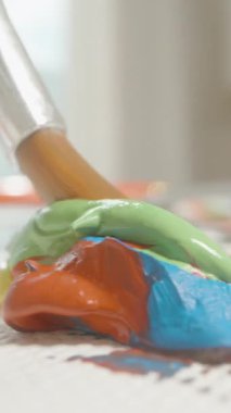 Dikey video. Dolly Kaydırma Hareketi ve Arkaplanda Işık, Renk Karıştırma Konsepti ile Makro Görünümdeki Tablo Üzerine Yeşil ve Mavi Boya Yığını