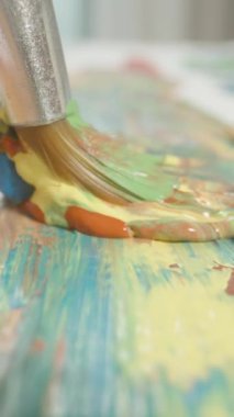 Dikey video. Dolly Kaydırma Hareketi, Renk Akımı Konsepti ile Makro Yakın Çekimde Boya Fırçası Mavi Sarı Turuncu Karışımı Çekiyor