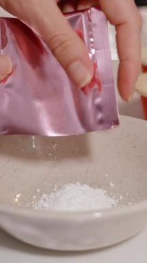 Dikey video. Pembe Foil Paketinden Beyaz Toz 'u Kırmızı Tutacaklı Kekler, Yakın Görünüm, Pişirme İçindekiler Konsepti ile çevrili Seramik Kaseye Dökmek