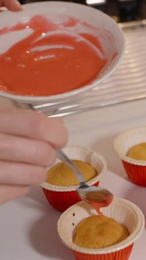 Dikey video. El Tutma Kaşığı Çiselemeli Pembe Buzlu Kek Kırmızı Holder 'da, Beyaz Tezgâh' ta Dekorasyon Konsepti, Kapalı Görüş, Birkaç Dekorasyon Kekiyle