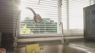 El Açılması Esnek Musluk ve Su Çıktıktan Sonra Musluk, Paslanmaz Çelik Lavabo 'da Güneş Işığı Parıltısı, Göz Seviyesi Açısı, Su Kısmi Konsepti