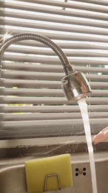 Dikey video. El musluğu açıp musluğu tıkırdatmak ta ki su nihayet mutfağa girene kadar. Güneş ışığı perdelerle, göz hizindeki açıyla, su basıncı iyileştirme konseptiyle.