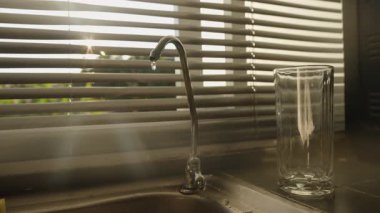 Süzgeç musluğundan damlayan su El, Valfı Sıkıca Kapatmak İçin Döndürürken, Güneş Işığı Perdelerden, Göz Seviyesi Açısı, Su Tasarruf Konsepti