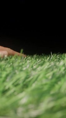 Dikey video. Koyu Arkaplan Dokunuşu ve Sentetik Doğa Konseptine Karşı Görünür Temas ve Dokunsal Etkileşim Sağlayan Yapay Yeşil Çimenin Yakın Çekimi
