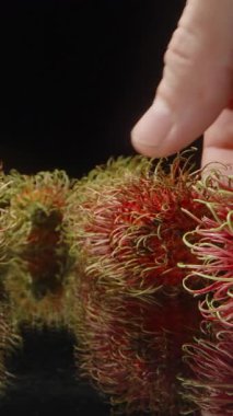 Arka planda Stüdyo Işığı Altında Diğer Meyvelerle Yansıtıcı Yüzeyden Nazikçe Dikenli Kırmızı Rambutan Meyveleri Alınıyor