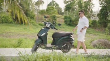 Beyaz Giysili Adam Koyu Yeşil Scooter Kırsal Yol 'da, Ağaçlar ve Çimenli, geniş açılı, Tropikal Keşif Konsepti