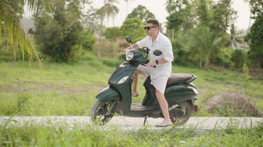 Beyaz Gömlekli Adam ve Kısa Şortlu Scooter Sürüyor Tropikal Ayar 'da Uzun Yol, yan açı, Boş Zaman ve Yaz Seyahati Konsepti
