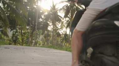 Scooter 'ı Kırsal Tropikal Yol' da Kickstand 'a yerleştirirken ve yerleştirirken Erkek Bacağının Yakın Çekimi, yumuşak güneş ışığıyla alçak açı, Yolculuğun Sonu