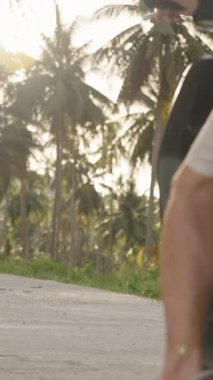 Dikey video. Scooter 'ı Kırsal Tropikal Yol' da Kickstand 'a yerleştirirken ve yerleştirirken Erkek Bacağının Yakın Çekimi, yumuşak güneş ışığıyla alçak açı, Yolculuğun Sonu