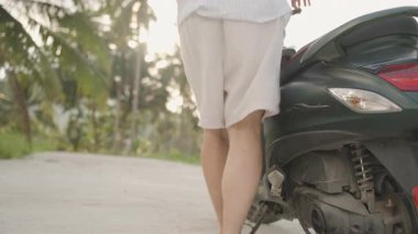 Beyaz Giysili Adam Yeşil Scooter 'la Virajlı Tropikal Yol boyunca gidiyor. Sığ alan derinliği, Ayrılış ve Özgürlük kavramına sahip arkadan yakın plan.