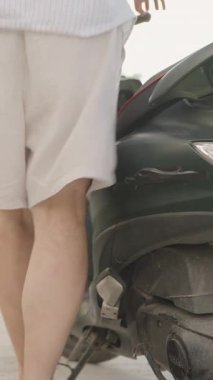 Dikey video. Beyaz Giysili Adam Yeşil Scooter 'la Virajlı Tropikal Yol boyunca gidiyor. Sığ alan derinliği, Ayrılış ve Özgürlük kavramına sahip arkadan yakın plan.